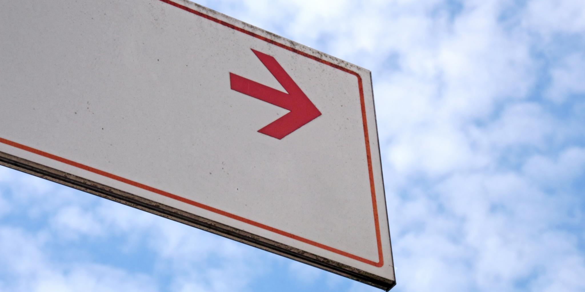 Bewölkter Himmel, Schild mit rotem Richtungspfeil