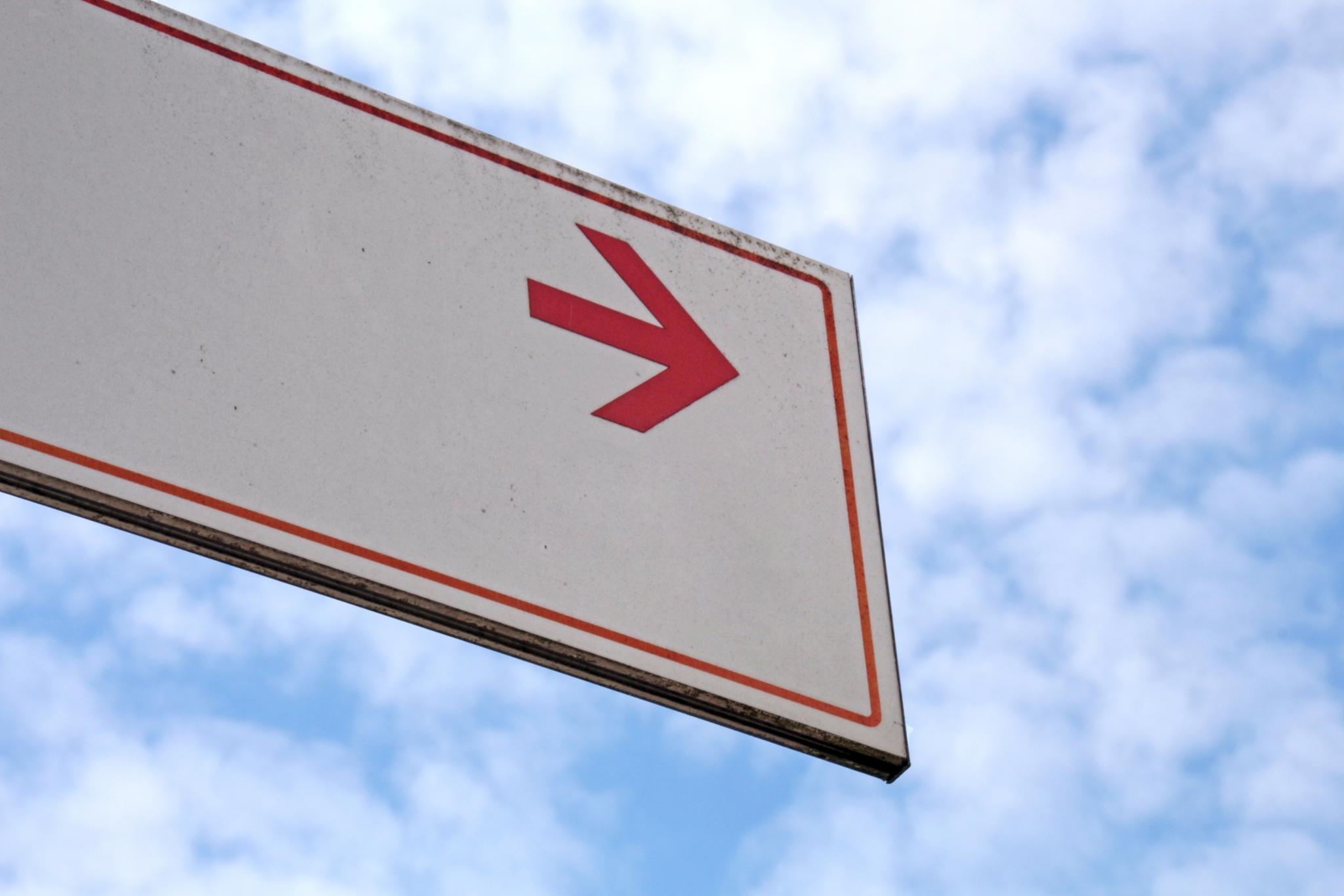 Bewölkter Himmel, Schild mit rotem Richtungspfeil